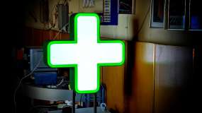 Готовый двусторонний световой аптечный крест 600 мм с белым фоном и зелёным свечением, вид с одной стороны