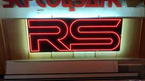 Интерьерный неоновый логотип RS, вид спереди во время тестирования в шоу-руме, красный LED неон и белая контражурная подсветка