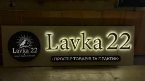 Включенная рекламная вывеска LAVKA 22 с контражурной подсветкой плоских букв и световыми лайтбоксами в темной мастерской