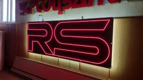 Інтер’єрна неонова вивіска RS, вигляд справа під кутом три чверті під час тестування у шоу-румі